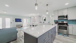 A modern kitchen with white cabinetry, a large island, stainless steel appliances, and pendant lighting.