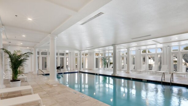 An indoor swimming pool with clear water, surrounded by white columns and seating areas.