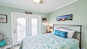 A bedroom with a bed, a chair, a door, and a wall with a 'Beach' sign.