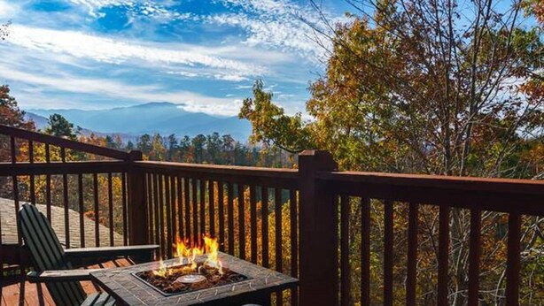 An outdoor deck with a fire feature, seating, and a view of trees and mountains.