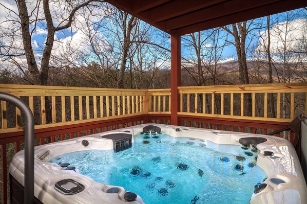 A hot tub with a wooden deck and a view of trees and mountains.