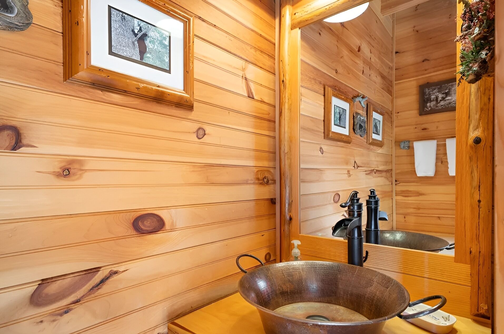 A wooden cabin interior with a large mirror, wooden walls, a metal basin, and a sink.