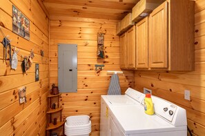 Una cabaña de madera pequeña con lavadora, un tendedero y un estante con varios objetos.