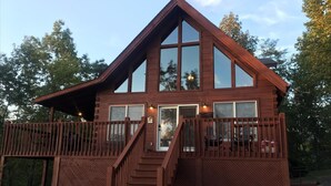 A two-story wooden cabin with a balcony, a staircase, and a small porch area.