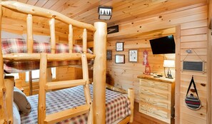 Una cabaña de madera con una cama litera, un escritorio pequeño y un televisor.