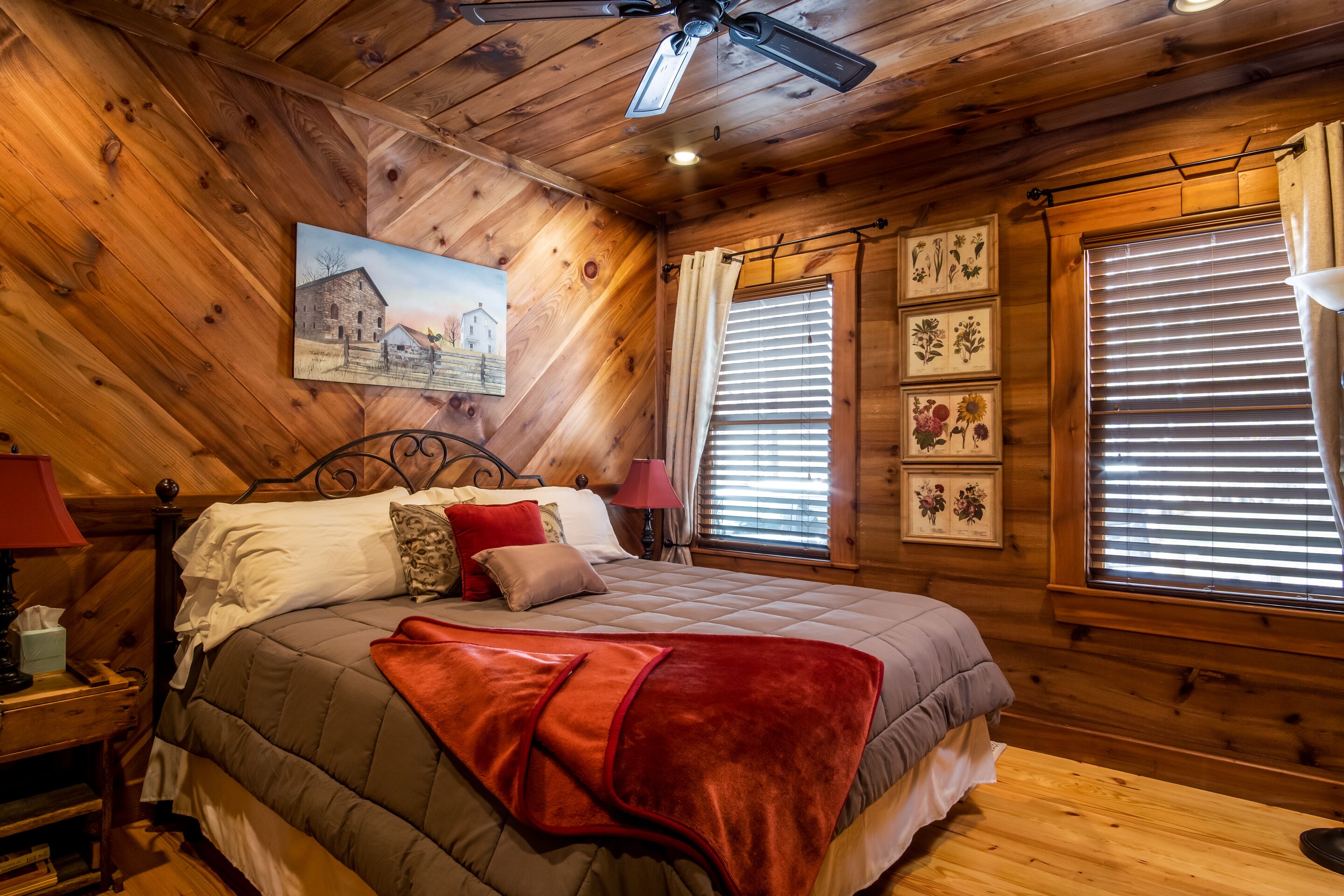 Ein Schlafzimmer einer Holzhütte mit einem Bett, einem Deckenventilator und einem Bild an der Wand.