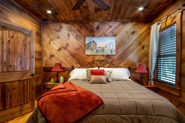 A wooden-paneled bedroom with a bed, two bedside tables, and a painting on the wall. - Amazing Luxury Getaway ~ 50 Feet on the Toccoa River ~ Great Fishing (BLUE RIDGE)
