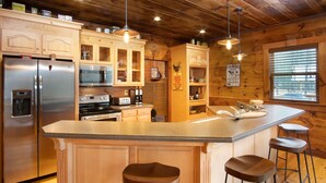 A kitchen with wooden cabinets, a stainless steel refrigerator, a built-in oven, a sink, and bar stools.