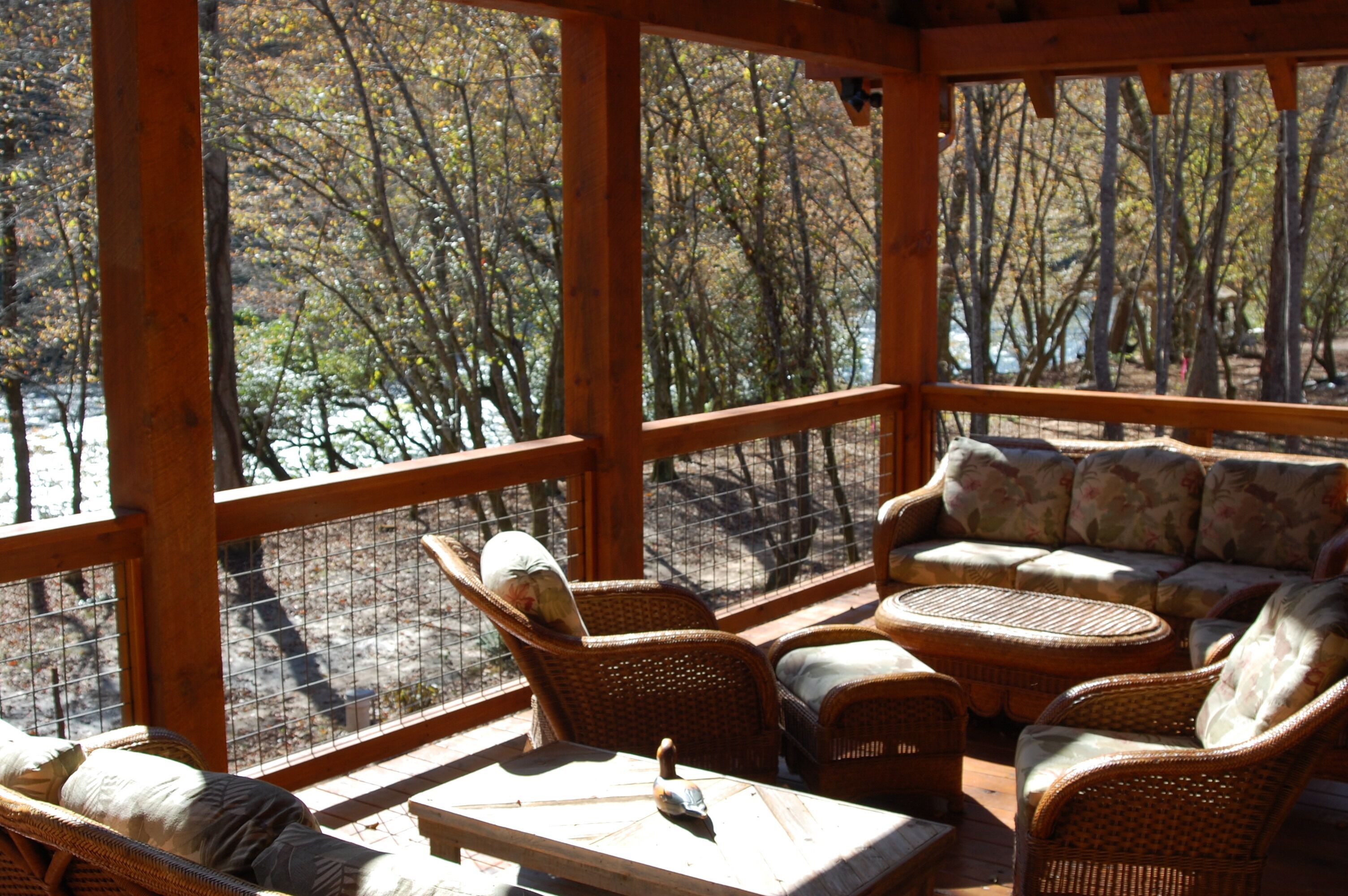 A covered outdoor seating area with wicker furniture and a view of a forested area.