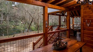 A wooden cabin with a wooden deck, a staircase, and a dining area with a table and benches.