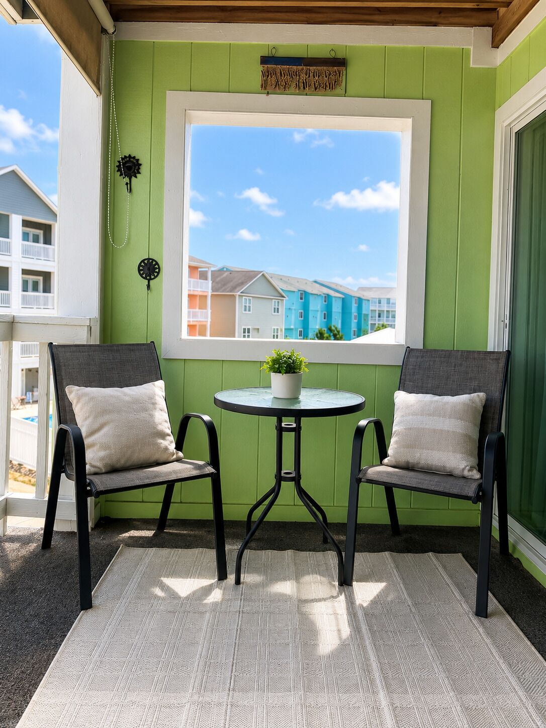 Ein Balkon mit zwei Stühlen, einem kleinen Tisch mit Pflanze und Blick auf farbenfrohe Häuser.