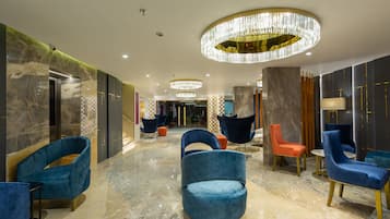 A lobby with marble flooring, blue and orange chairs, and a large chandelier.