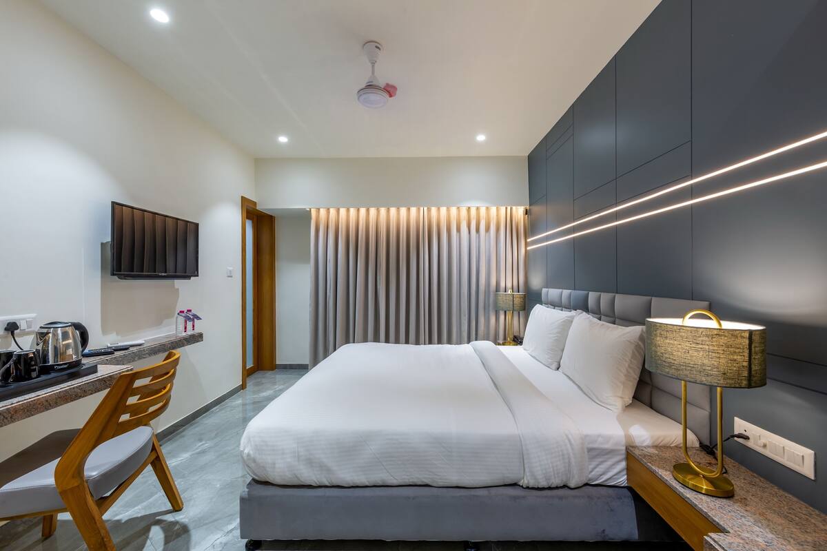 A modern hotel room with a bed, desk, chair, and a TV.