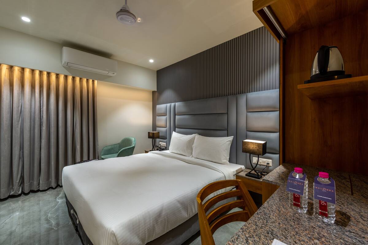 A hotel room with a large bed, a wooden headboard, a desk with a chair, a water bottle, and a coffee maker.
