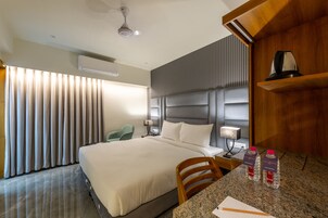 Una habitación de hotel con una cama grande, un escritorio con silla, una botella de agua y una cafetera.