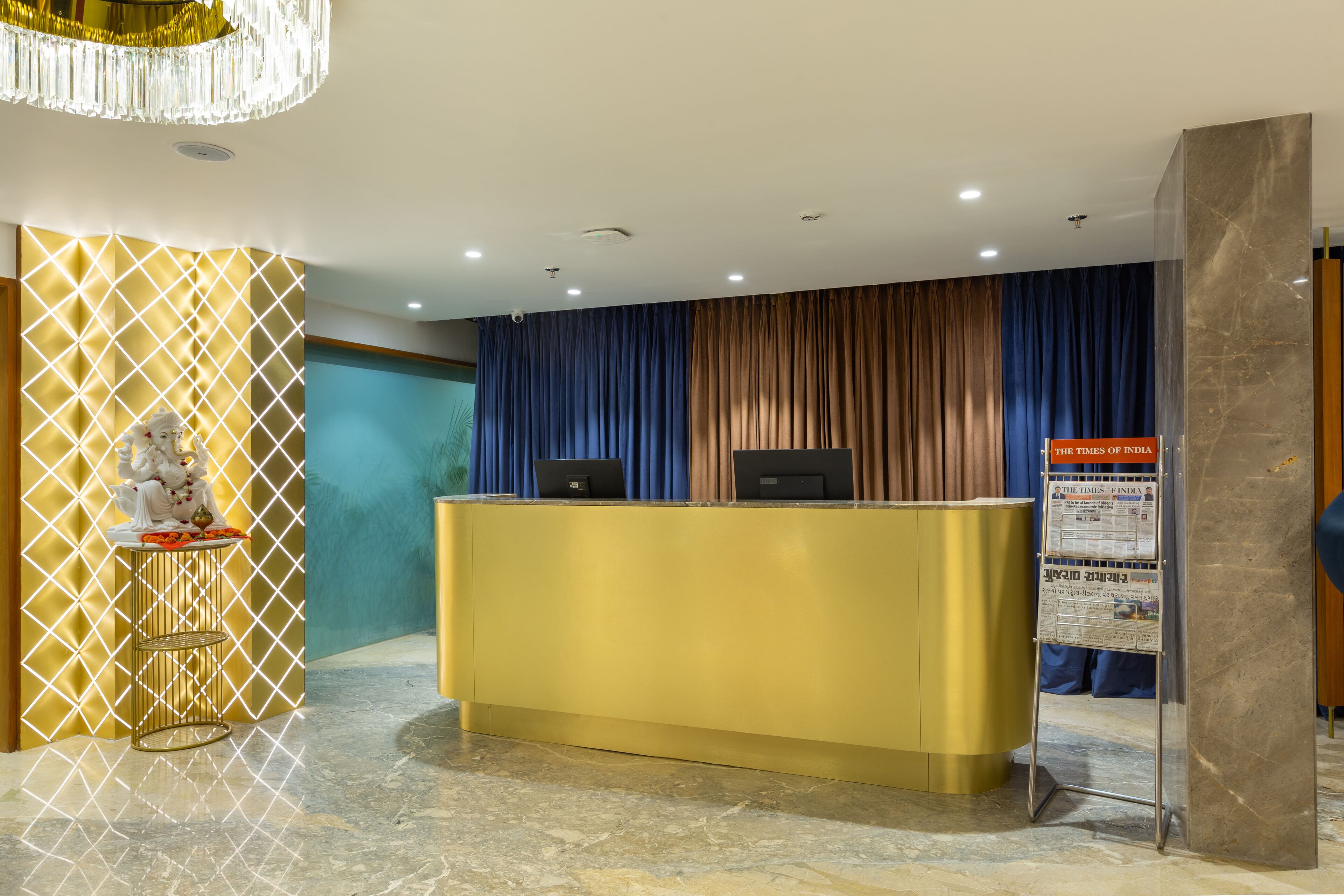 A reception area with a gold reception desk, a newspaper stand, and a statue on a pedestal.