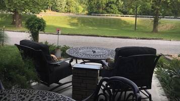 An outdoor patio with a round table and four chairs, surrounded by greenery and a view of a road.