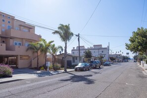 Eine Wohnstraße mit Häusern, parkenden Autos und Palmen.
