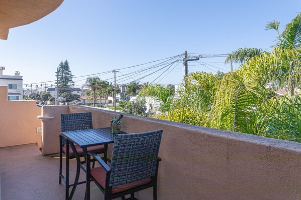 A balcony with a table and chairs, overlooking a residential area with houses and palm trees. - Prime Downtown Location, Walk to the Beach! Home Away from Home! (Pismo Beach)