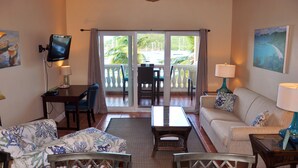 Une chambre d’hôtel avec un balcon, une télévision, un canapé, une table à manger et un ventilateur de plafond.