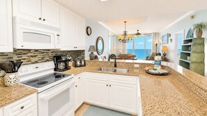A kitchen with white cabinets, a microwave, stove, and coffee maker. There is a view of a balcony with a chair and a plant.