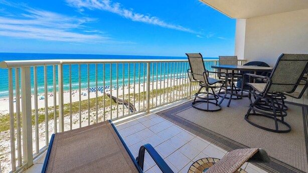 A balcony with a view of the beach, a table with chairs, and a small rug.
