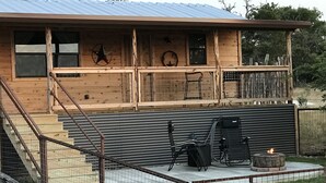 A wooden cabin with a metal roof, a fenced patio area, and a fire pit. - New lower rates. Great reviews   Elevated deck, Pet friendly, Romantic scenic (Fredericksburg)