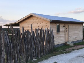 A wooden cabin with a sloped roof, a small porch, and a wooden fence.