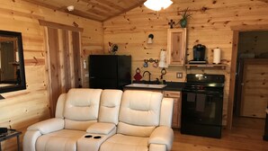 A cozy log cabin interior with a reclining sofa, a kitchen area, and wooden walls. - New lower rates. Great reviews   Elevated deck, Pet friendly, Romantic scenic (Fredericksburg)