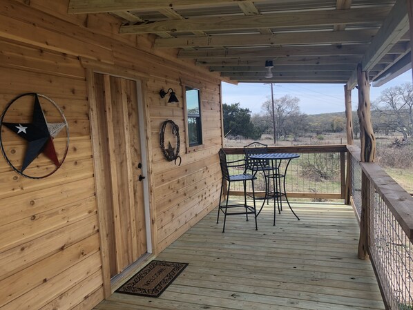 A wooden porch with a metal table and chairs, a star decoration, and a welcome mat.