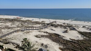 Une plage avec une promenade en bois menant à l’eau, des dunes de sable et une vue dégagée sur l’océan.