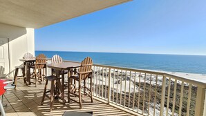 Un balcon avec une table et des chaises, donnant sur une plage et offrant une vue dégagée sur l’océan.