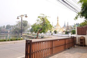 Vista da rua com um templo ao fundo, uma cerca de metal e uma árvore.