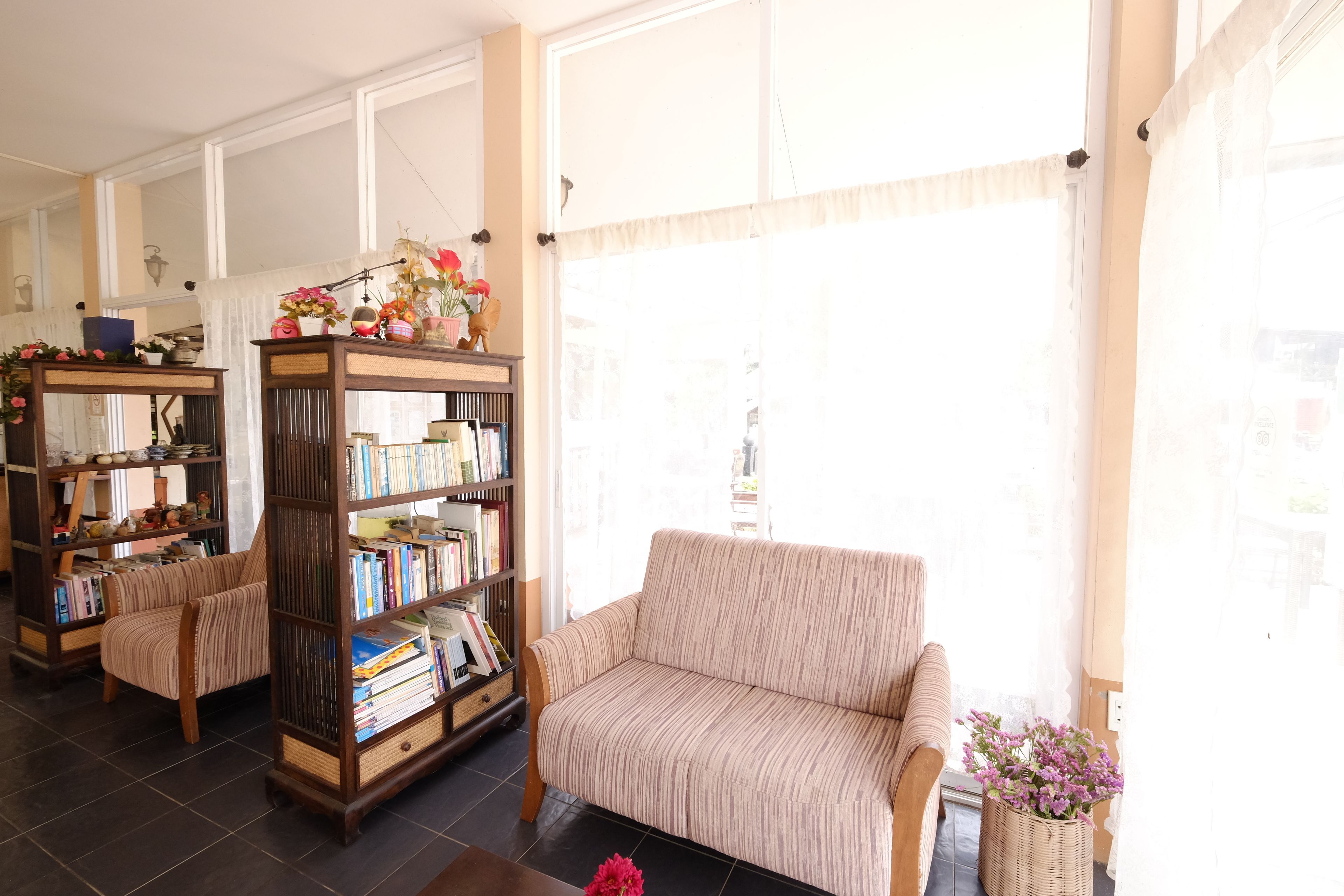 A living room with a striped sofa, a tall bookshelf, and a window with sheer curtains.