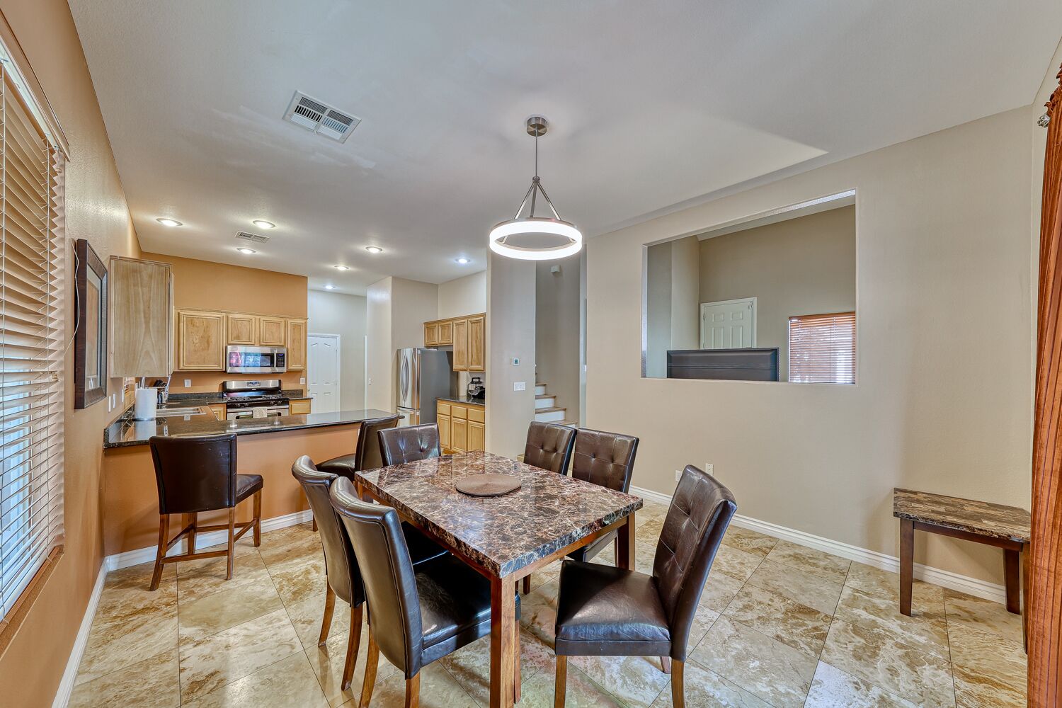 A spacious dining area with a marble table and leather chairs, a kitchen with wooden cabinets, and a modern pendant light.