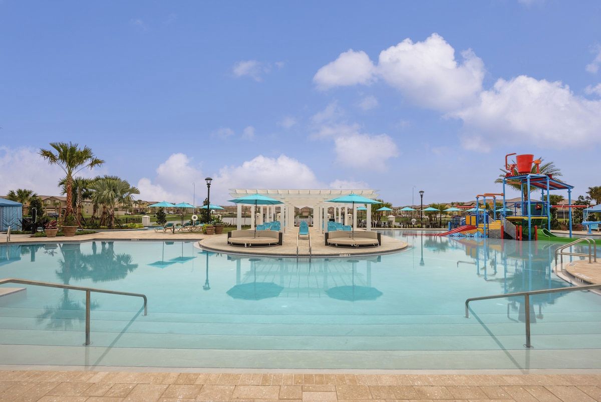 Una piscina con sillones de playa y sombrillas, rodeada de palmeras y un cielo despejado.
