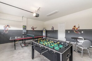 Et værelse med et fodboldbord, et ping pong bord og en projektor monteret i loftet.