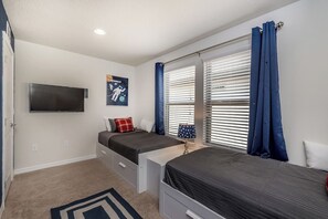 Une chambre à coucher avec un lit, une télévision, une fenêtre avec des stores et une affiche accrochée au mur.