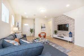 A modern living room with a grey sofa, a coffee table, and a TV mounted on a stone-textured wall. - Vacation Home: 6BR w/ Pool + Game Room near Disney (Kissimmee)