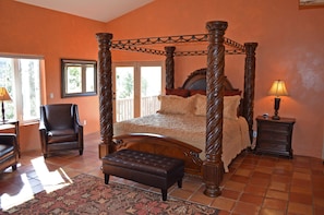 A four-poster bed with a wooden headboard, a bench, a chair, and a nightstand with a lamp.