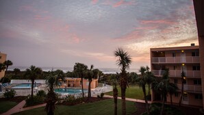 A hotel with a pool, palm trees, and a view of the ocean at sunset.