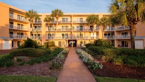 A multi-story hotel with balconies, a central walkway, and landscaped gardens.