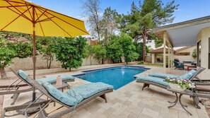 Un jardin avec une piscine, des chaises longues et un parasol jaune.
