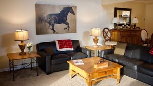A living room with a black leather sofa, two wooden side tables with lamps, a coffee table, and a large painting of a horse on the wall. - 3 BR/BA End Unit, Lg Decks, Views (Sun Valley)
