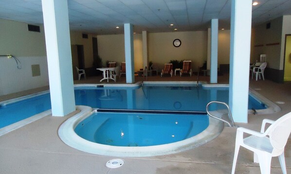 Una piscina interior con una bañera de hidromasaje, rodeada de sillas y mesas blancas.