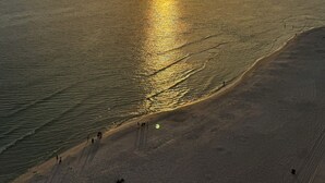 Ein Strand bei Sonnenuntergang über dem Meer, eine sandige Küste und einige Spaziergänger.