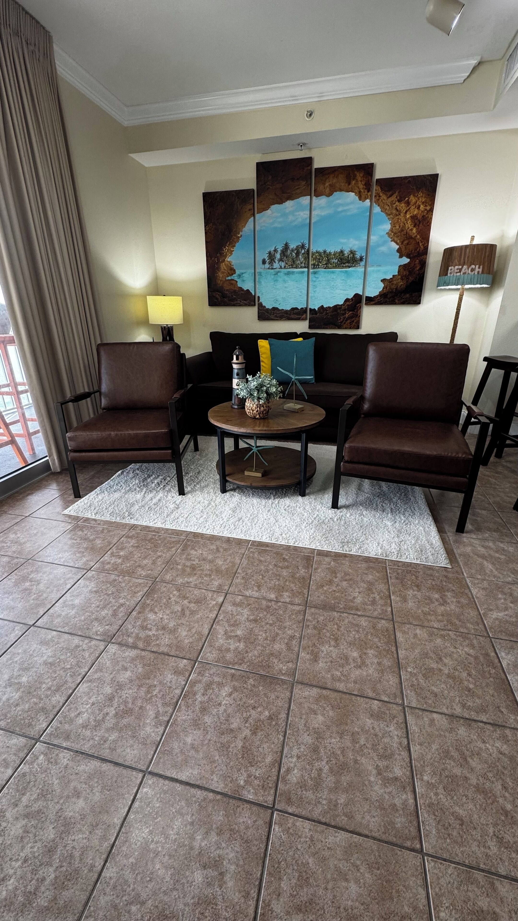 Un salón con dos sofás de cuero marrón, una mesa de centro redonda con objetos decorativos, una lámpara y un cuadro grande con temática marina.