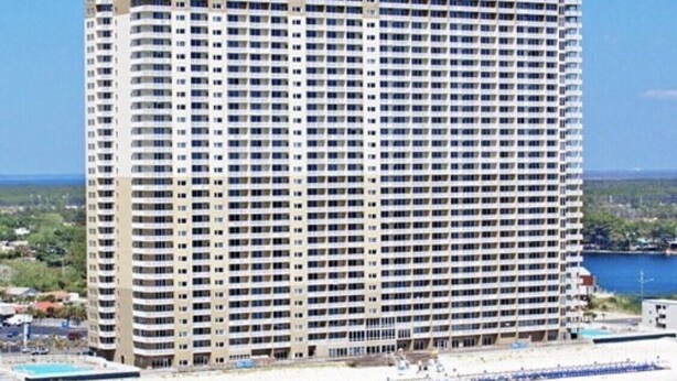 Ein hohes, mehrgeschossiges Hotel mit einheitlicher Fassade, nahe einem Strand mit Sandküste und einem Gewässer.