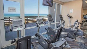 Ein Fitnessraum mit Cardiogeräten, einem Fernseher und Meerblick durch große Fenster.