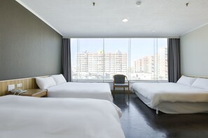 Habitación de hotel con dos camas, una silla, una mesita de noche con teléfono y un ventanal que ofrece vistas a la ciudad.